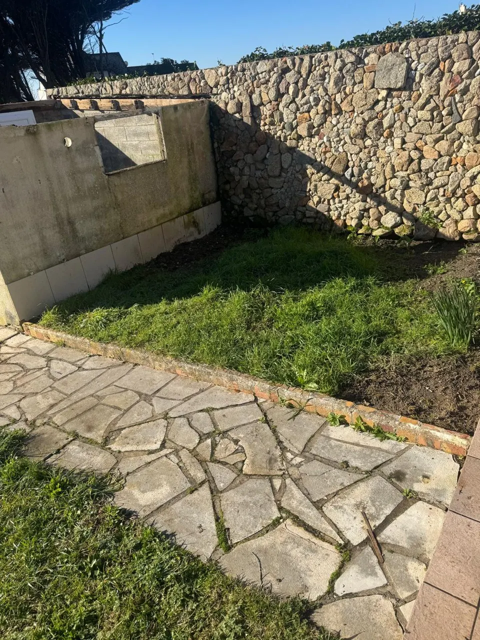 Jardin : dallage de pierre au premier plan, pelouse et mur en pierre au fond.