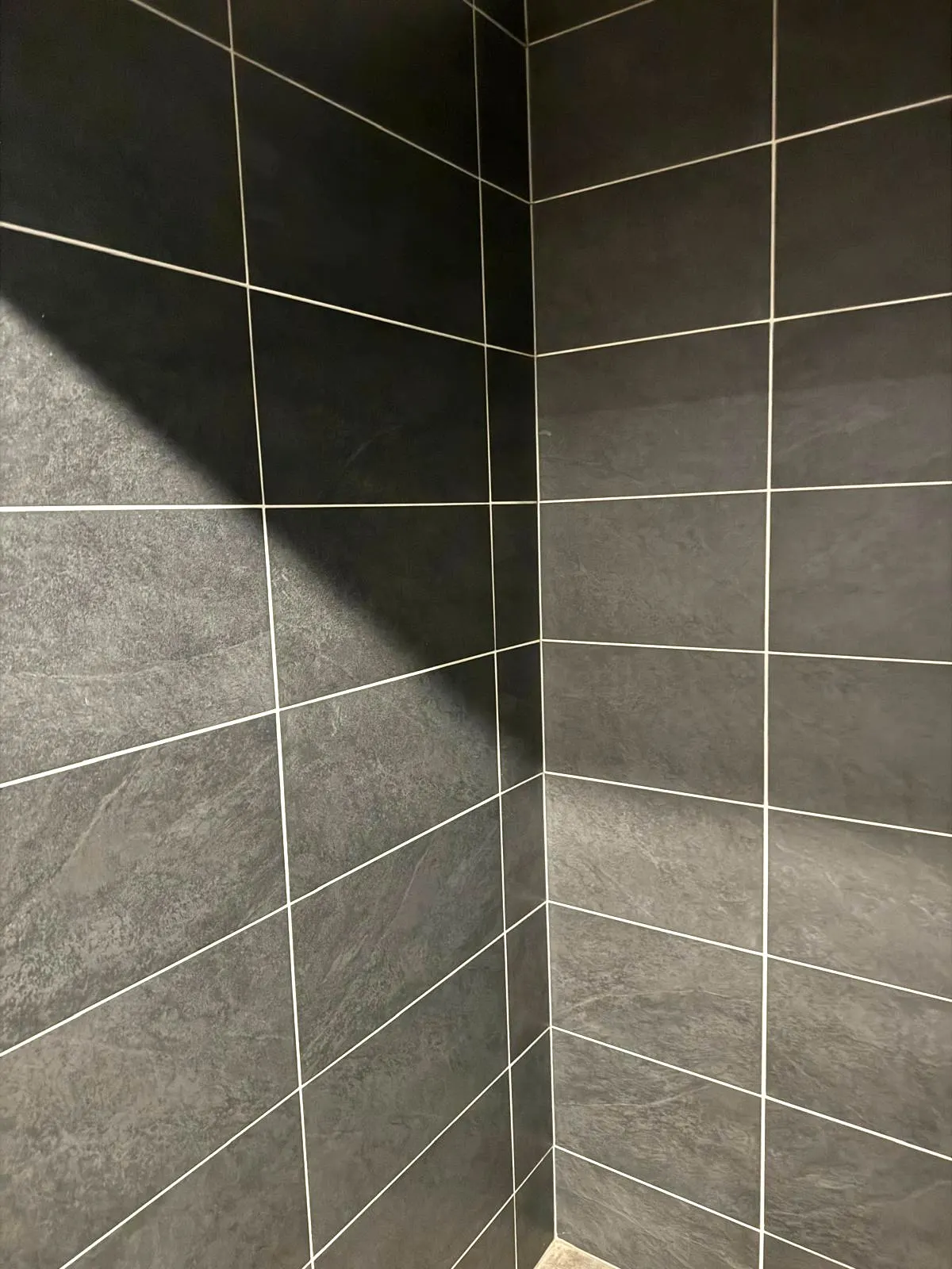 Angle de mur en faïence anthracite grand format, joints clairs alignés.