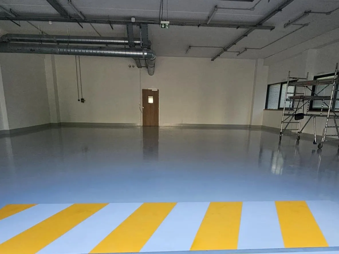 Atelier : sol coulé gris avec une bande de marquage jaune et blanche à l'entrée.