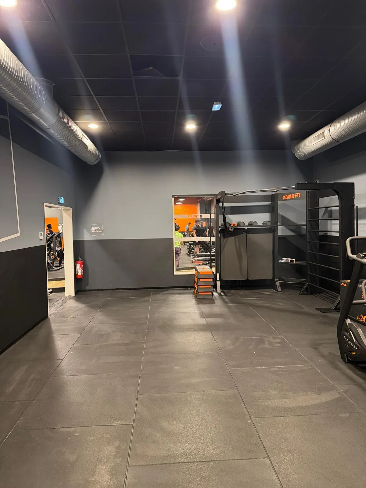 Salle de sport : carrelage gris grand format au sol, murs gris et noir, éclairage encastré.